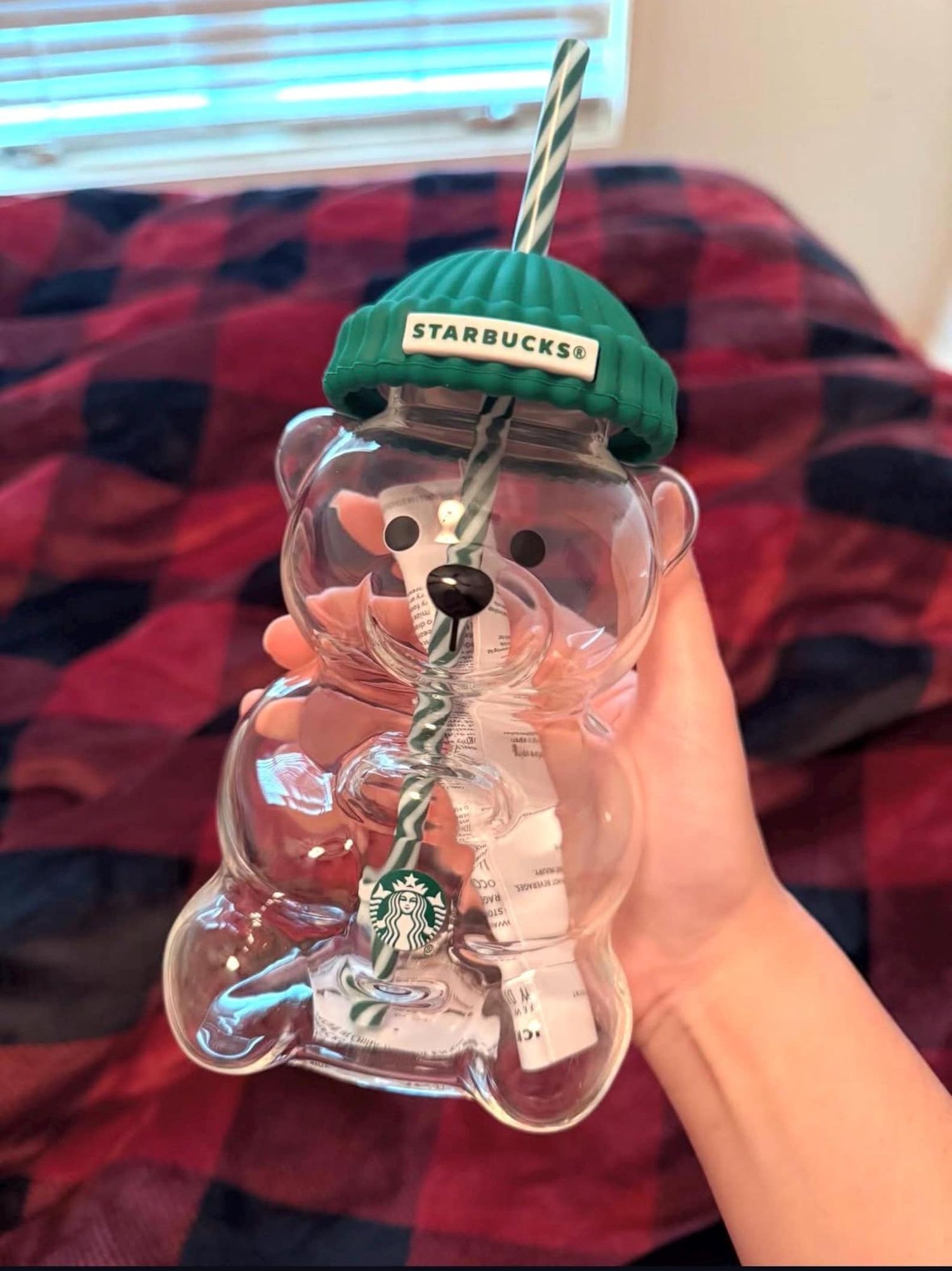 Clear bear-shaped Starbucks cup with green lid and straw on a red and black checkered background